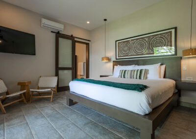 A king bed, two floating night stands with pendant lights above, and a small sitting area with a tv in the Oceano Suite.
